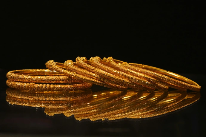 A stack of ornate gold bangles on a reflective surface.